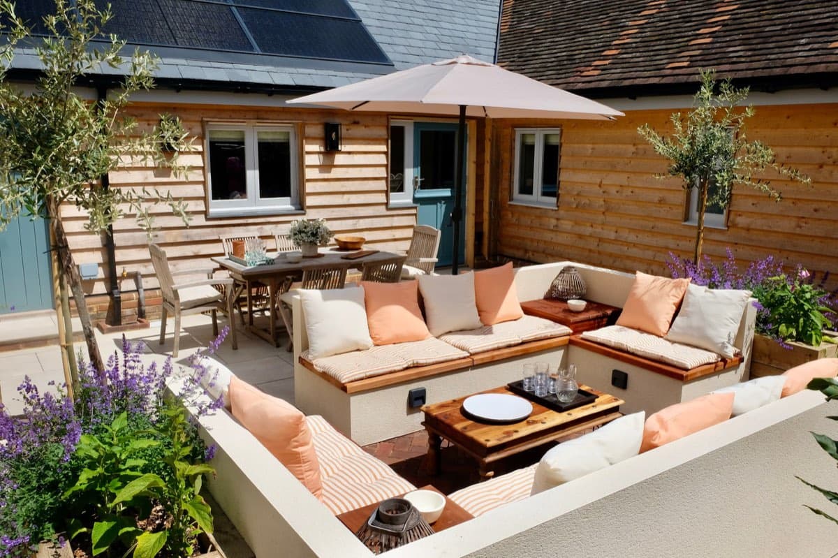 The barn's courtyard: timber walls, a corner sofa under a parasol, and a table set beyond it.