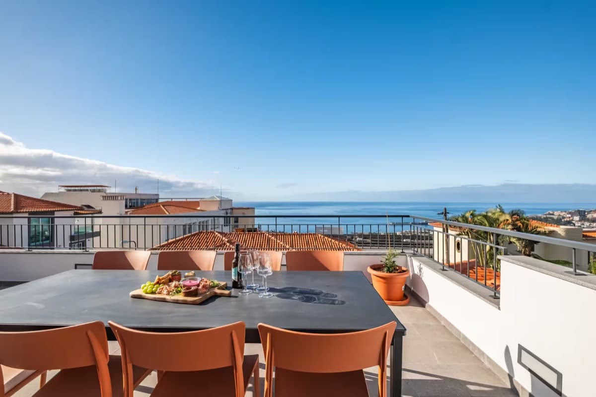 The terrace set for dinner, above the rooftops of Funchal at golden hour.
