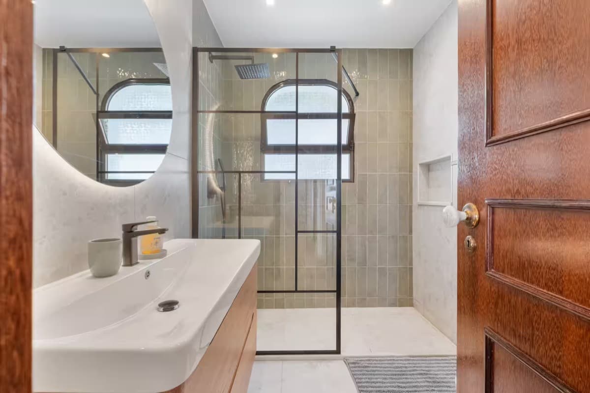 A tiled walk-in shower and washbasin beneath an arched window.