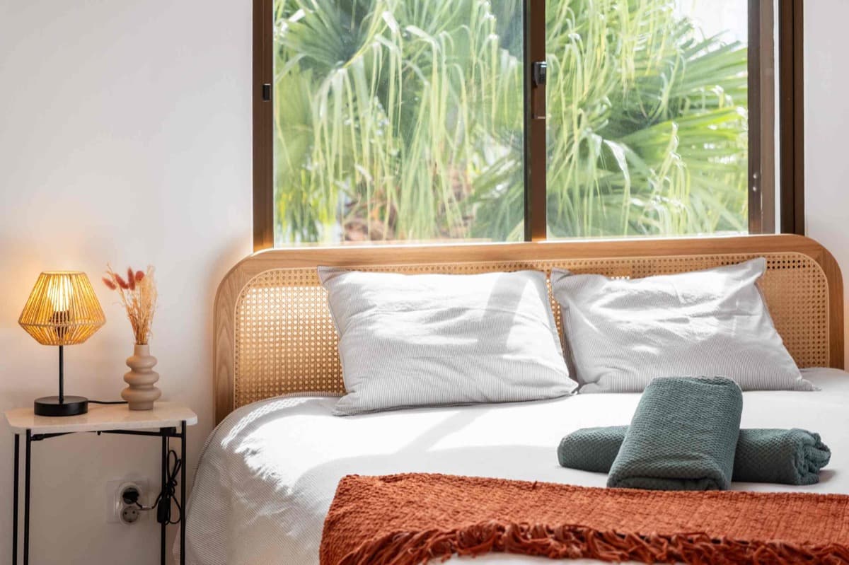 A bedroom with a cane headboard and a window onto the palms.